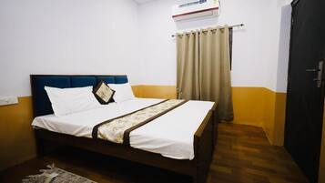 Una cama individual con cabecera, una mesita de noche, un tapete estampado, una ventana con cortinas y un equipo de aire acondicionado.