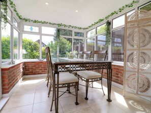 A conservatory with a glass table and chairs, brick walls, and large windows.