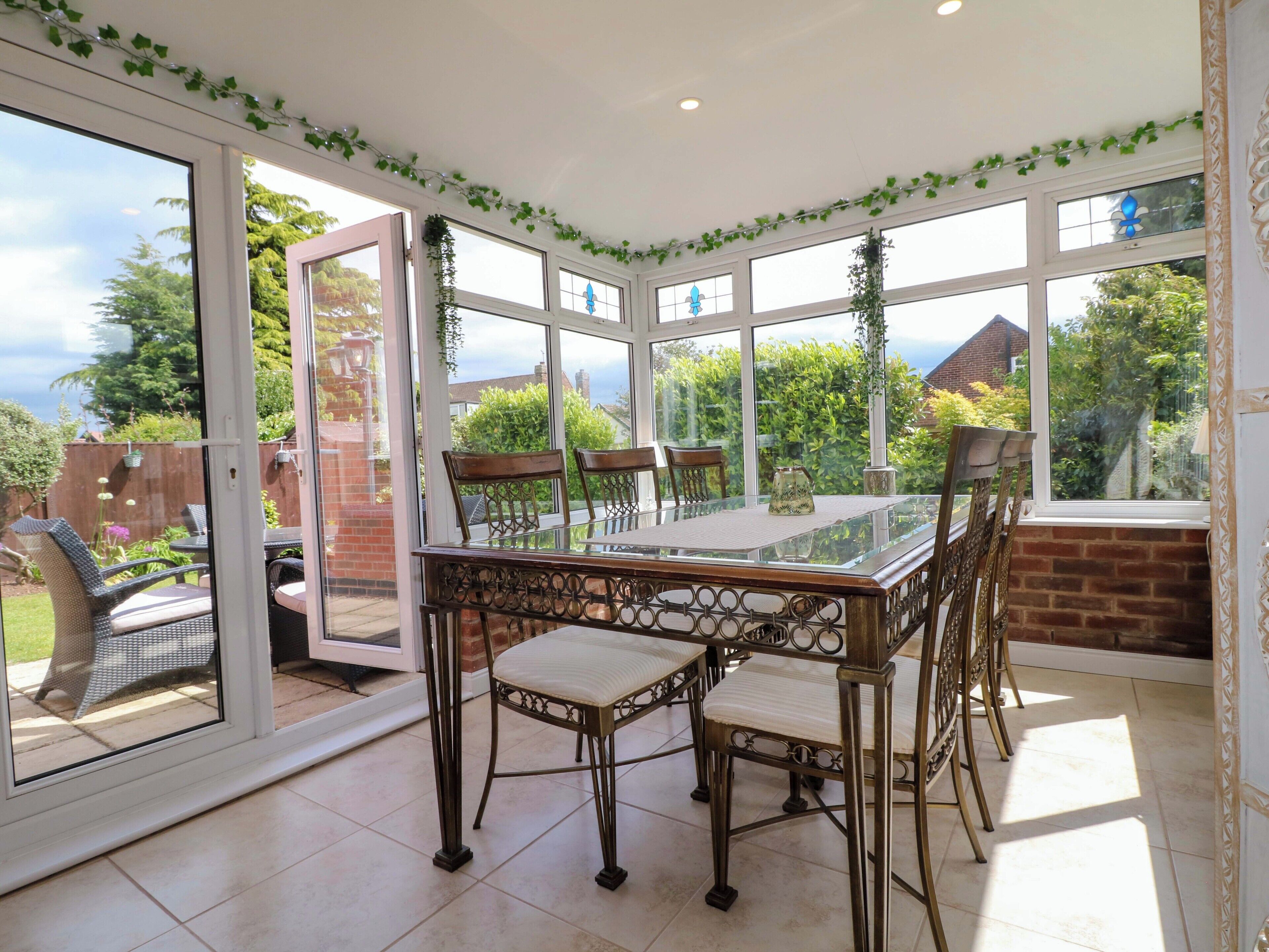 A conservatory with a glass table, chairs, and a view of the garden.