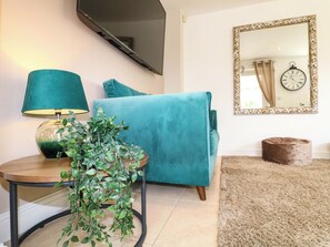 A teal sofa, a round wooden table with a green lamp, and a potted plant.