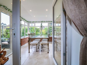 A conservatory with a glass door, a dining table, chairs, and a view of greenery outside. - The Haven (Nottingham)