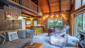 A cozy cabin interior with a sofa, armchair, wooden ceiling, and a fireplace. - Kennedy Mountain Chalet - AC & Pool Access! (Arnold)