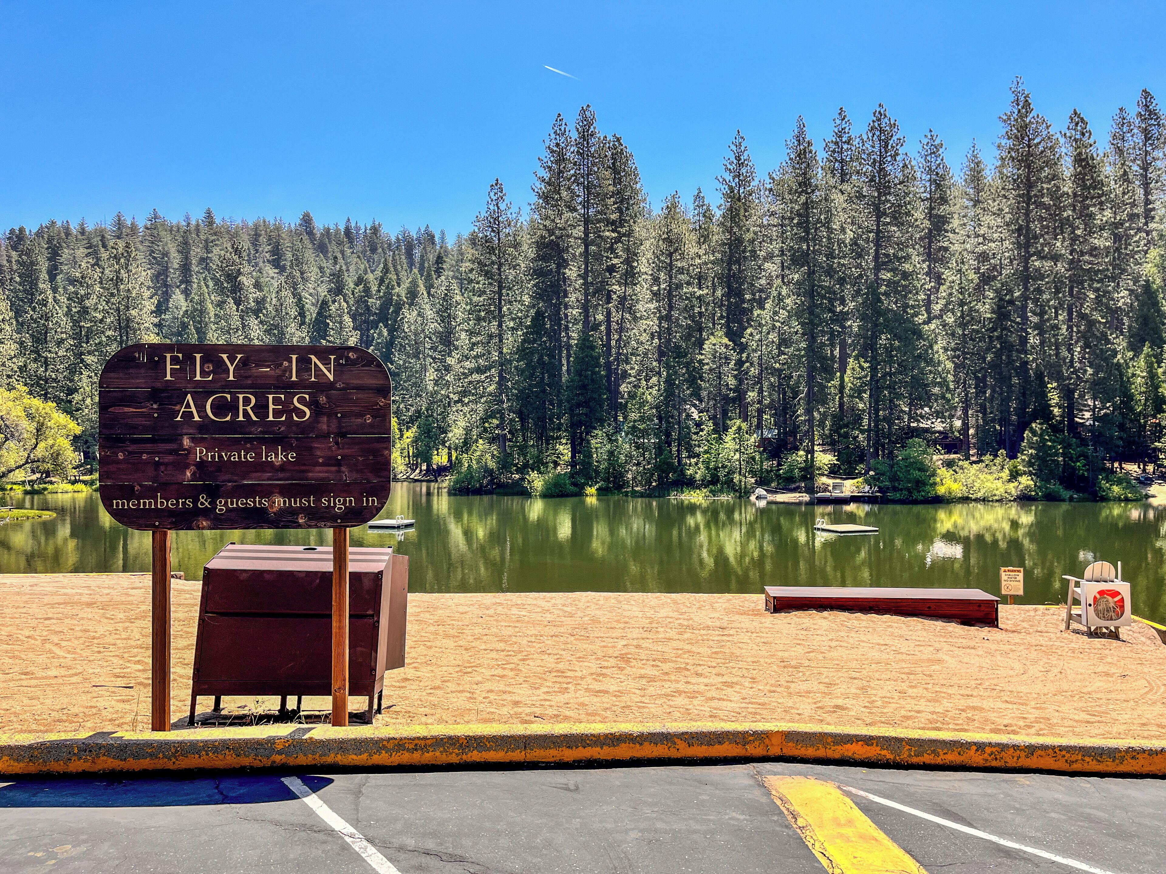 A fly-in acres sign at a private lake with a sandy beach and dock.