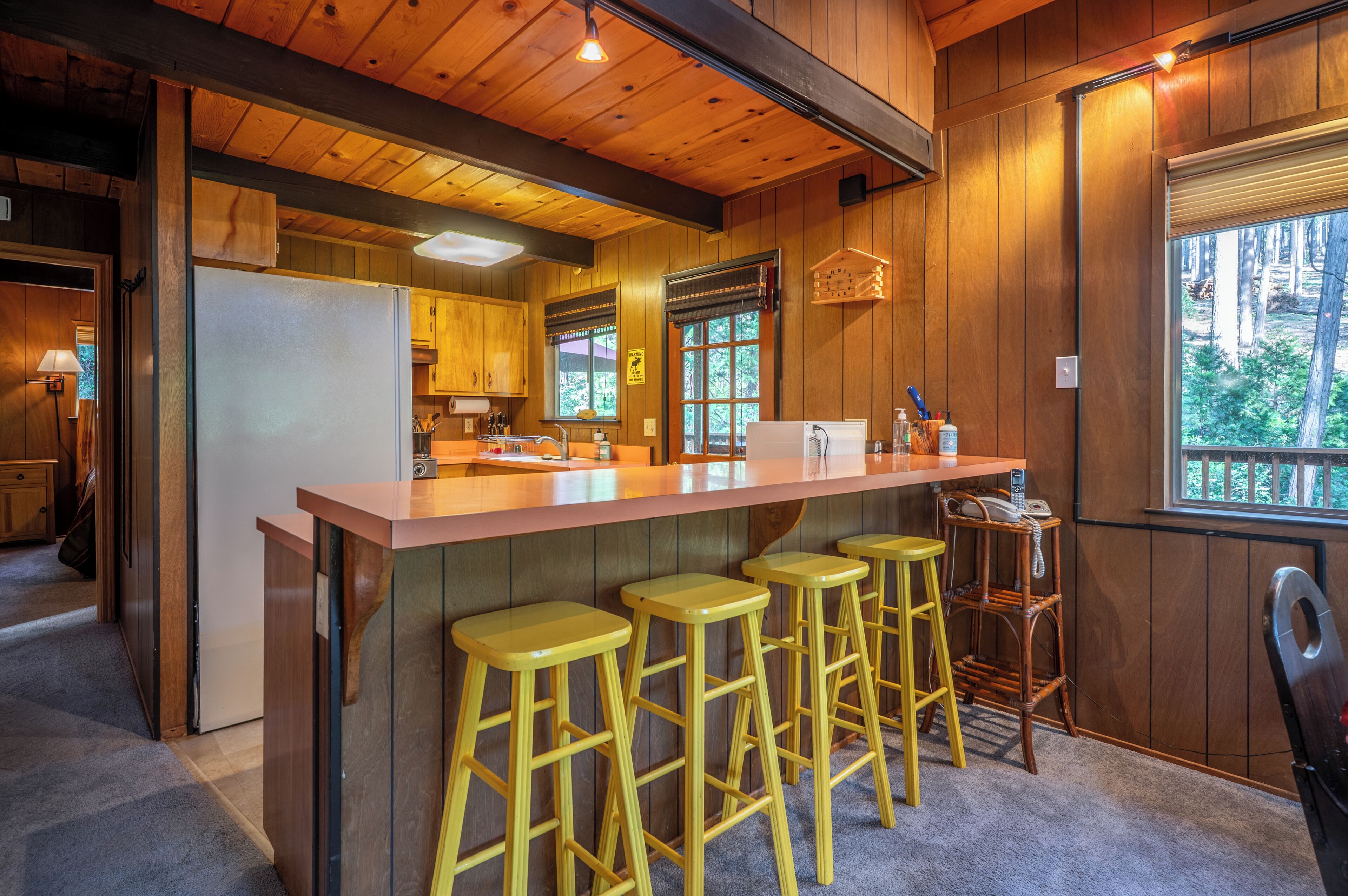 Une cuisine avec des lambris en bois, un îlot central avec des tabourets et une vue par la fenêtre.