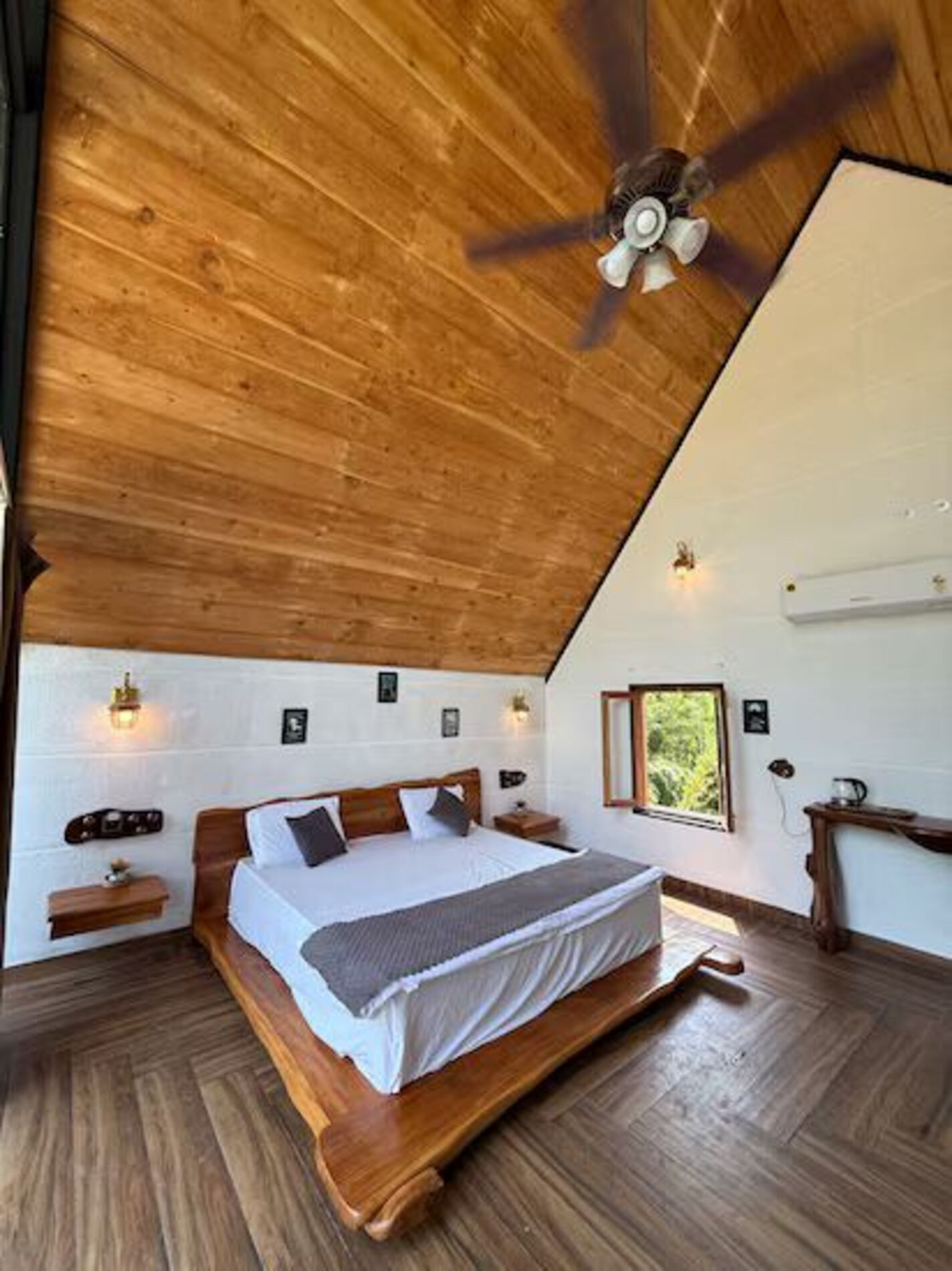 A bedroom with a wooden ceiling, a bed, bedside tables, wall-mounted lights, and a window.