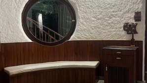 Una habitación con un banco curvo de madera, un ventanal redondo con barandilla metálica, un armario de madera y una pared con textura.