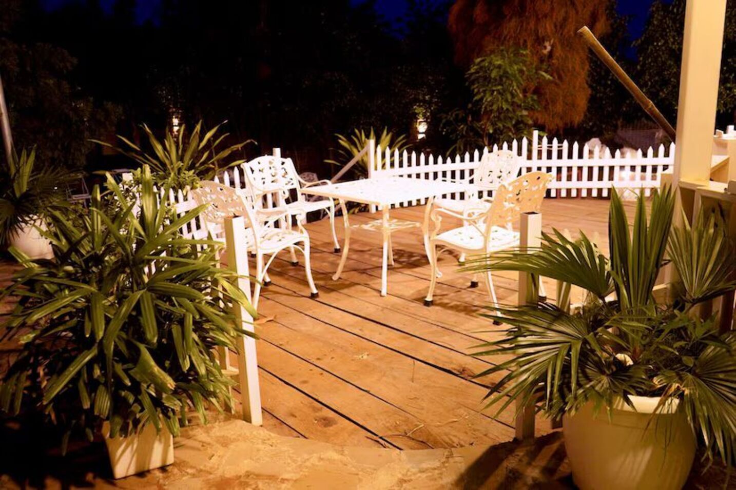 A wooden deck with white outdoor furniture, surrounded by potted plants.