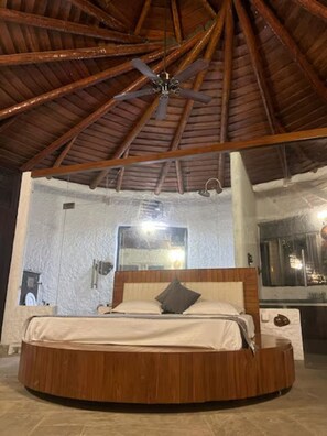 Una cama de madera redonda con cabecera, un ventilador de techo y un espejo grande en la pared.
