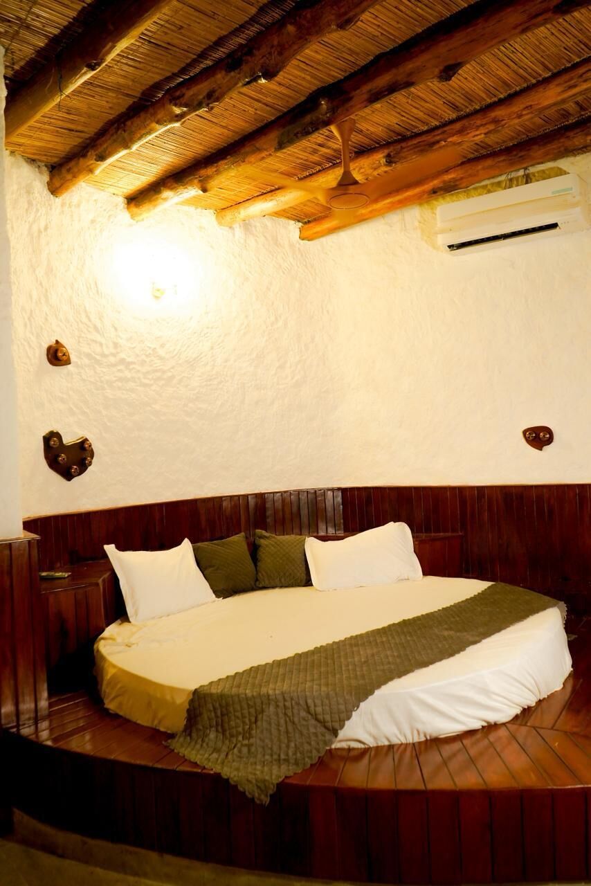A circular bed with a wooden headboard, a wall-mounted air conditioner, and a textured ceiling.