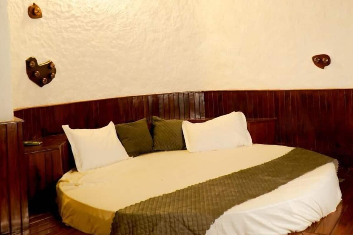 A circular bed with a wooden headboard, a wall-mounted air conditioner, and a textured ceiling.