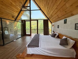 Un dormitorio con una cama grande, techo de madera y vistas a árboles a través de amplios ventanales.