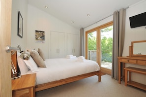 A bedroom with a bed, a wooden desk, a mirror, and a view of greenery outside. - 11 Water's Edge (Looe)