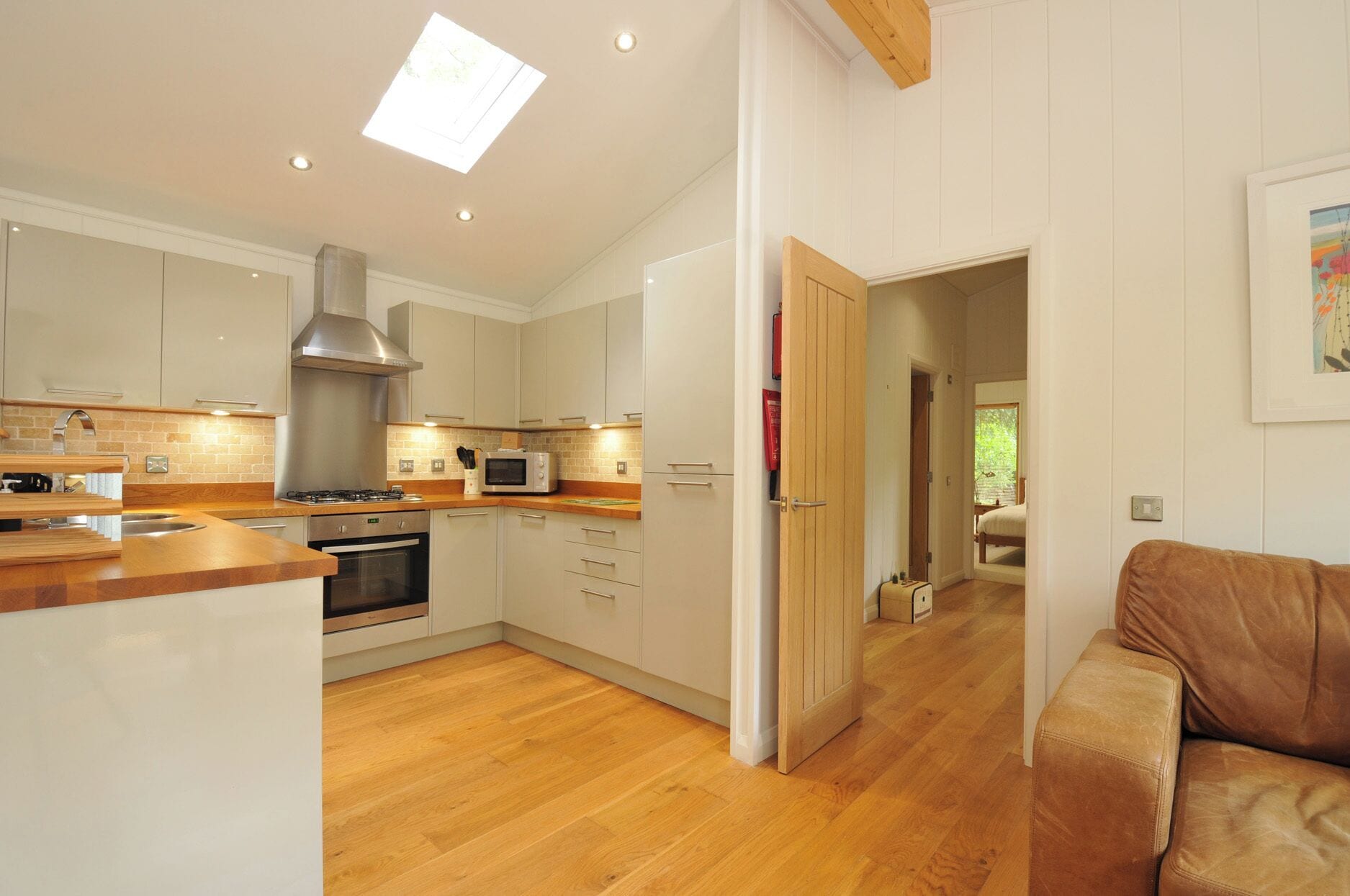 A modern kitchen with wooden flooring, a built-in oven, and a microwave.