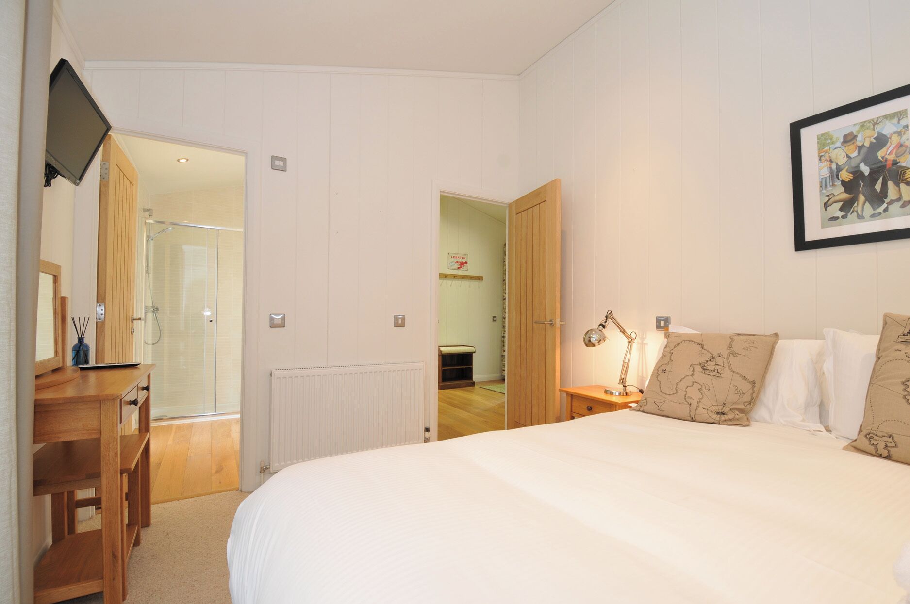 A bedroom with a bed, a desk, a chair, a lamp, and a framed picture on the wall.