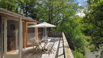 A wooden deck with a table and chairs, a glass door, and a view of a river.