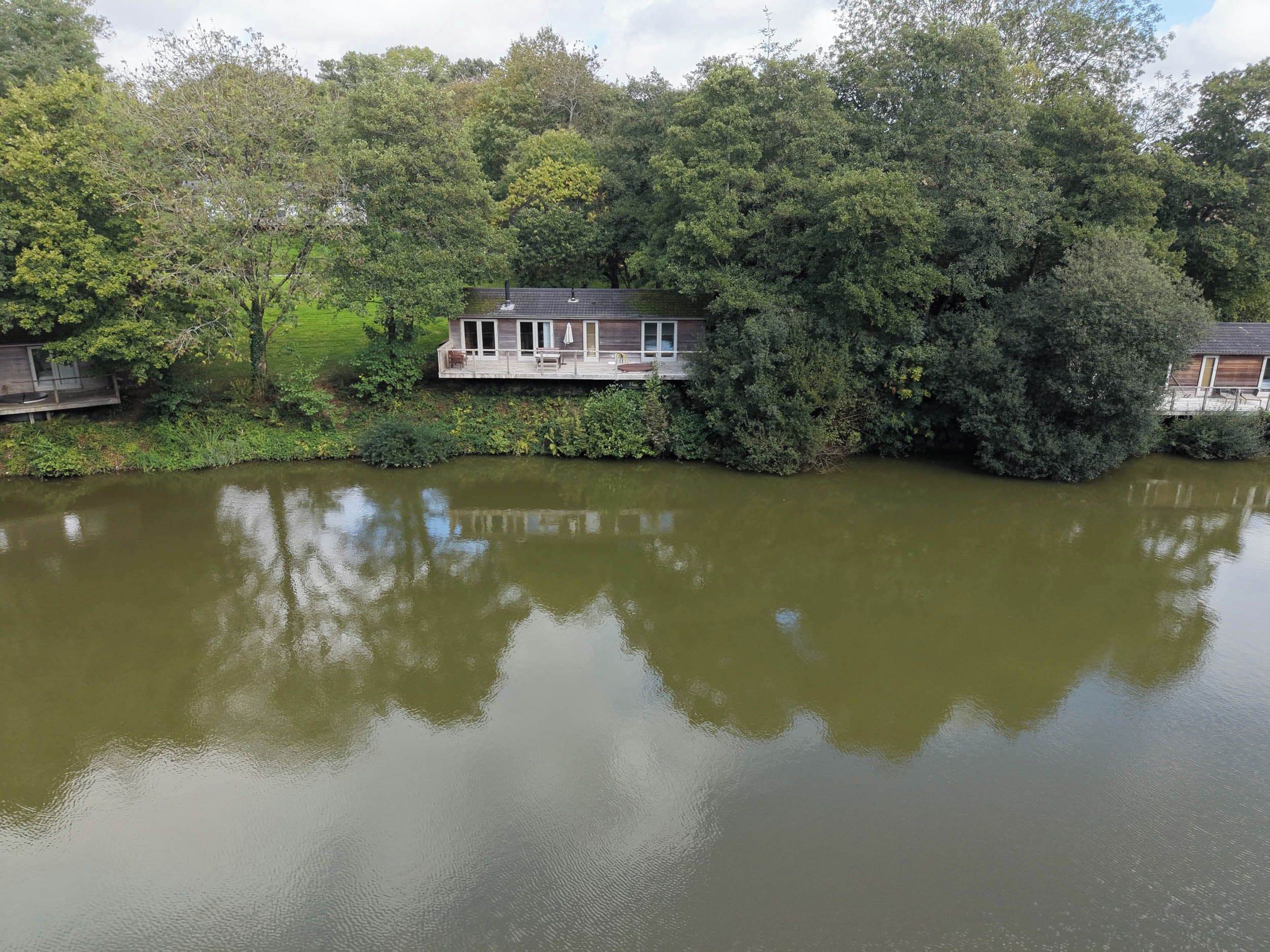 A lakeside house with a deck overlooking the water, surrounded by dense trees.