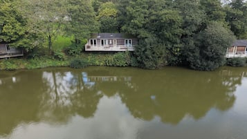 A lakeside house with a deck overlooking the water, surrounded by dense trees.