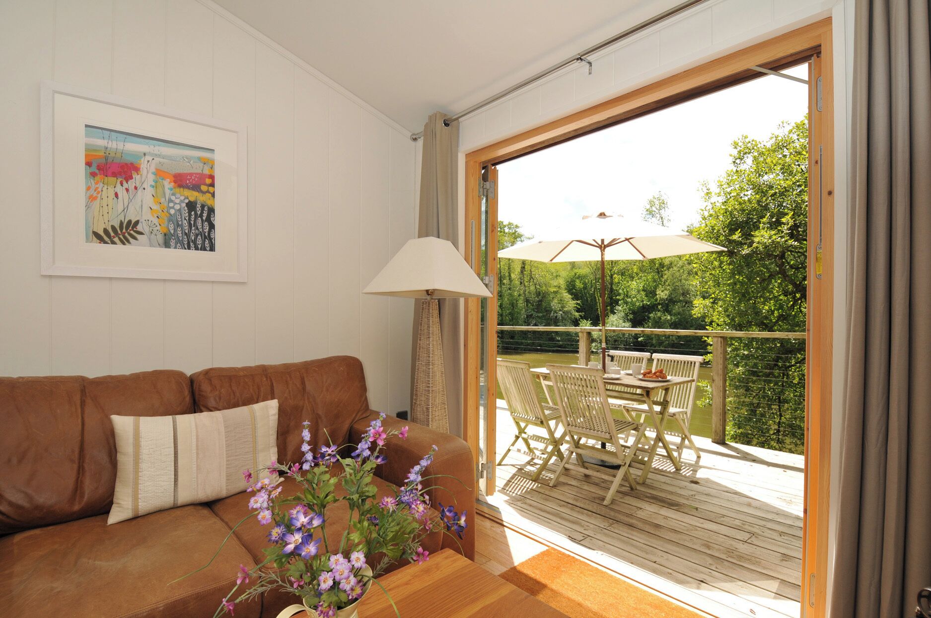 Una sala de estar con un sofá de cuero marrón, una lámpara blanca y una mesa de madera con mobiliario de exterior.