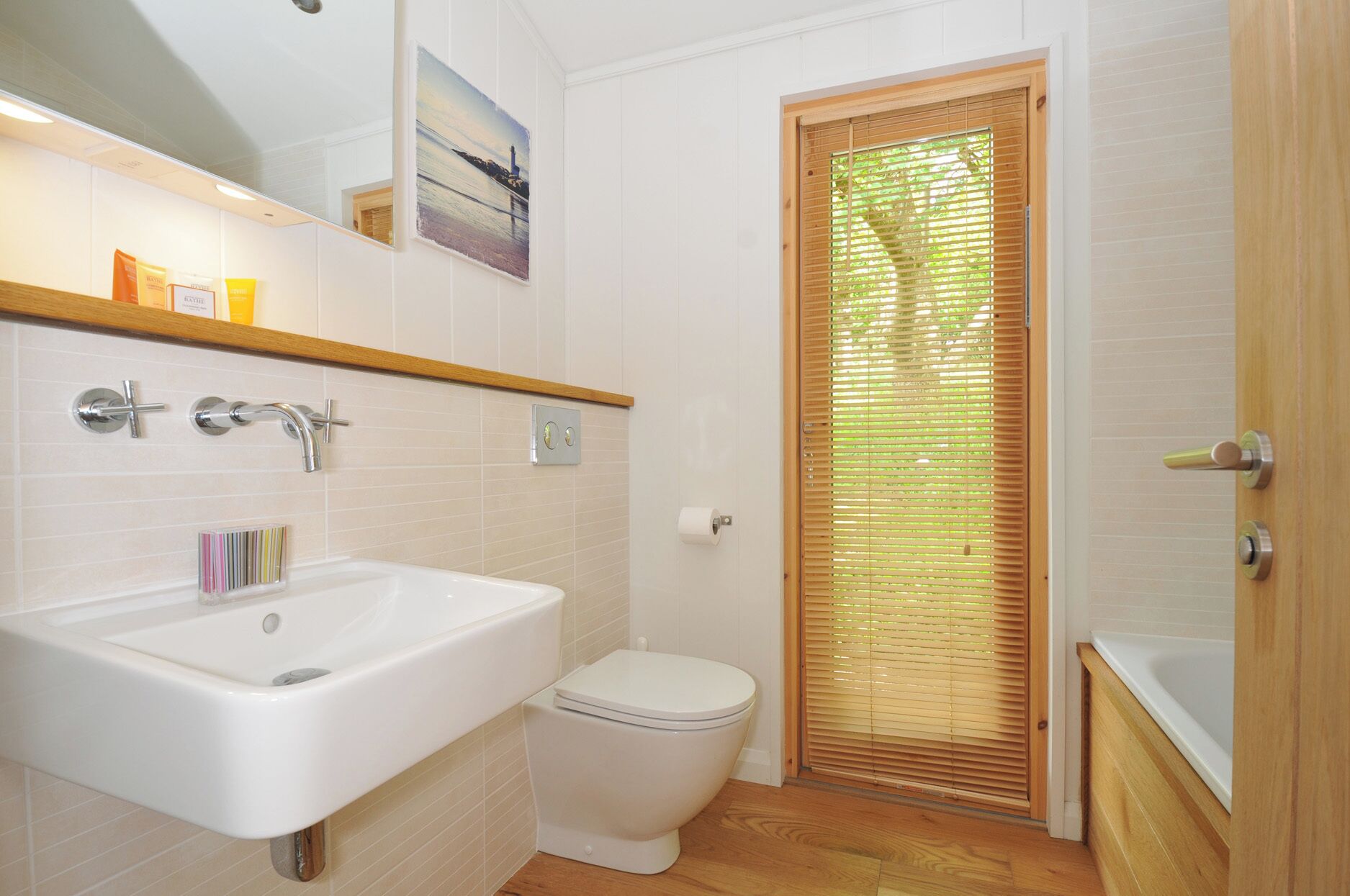 Une salle de bain avec un lavabo blanc, des toilettes et une porte en bois équipée de stores.