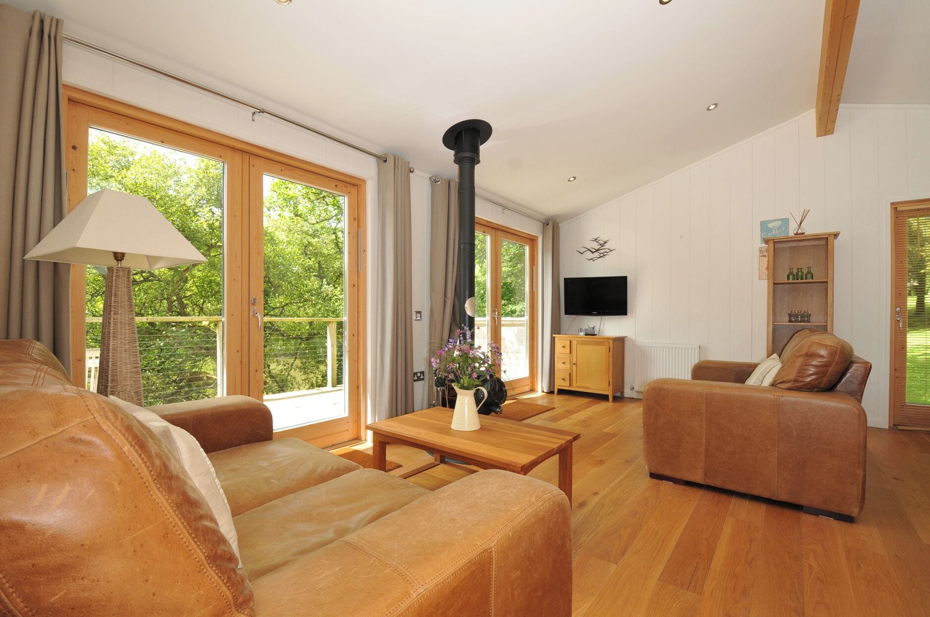 A spacious living room with leather sofas, a wooden coffee table, a TV, and a fireplace.