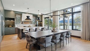 Een moderne keuken met een centraal eiland, een eetgedeelte met stoelen en grote ramen met uitzicht op de omgeving.