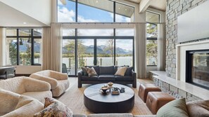 A spacious living room with a large window overlooking a lake, a fireplace, and a stone wall.