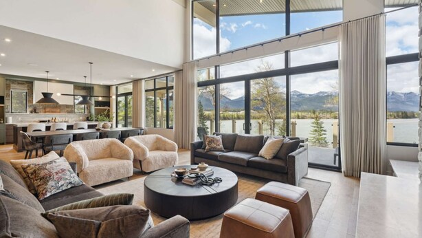 Een ruime woonkamer met een groot raam met uitzicht op een meer en bergen, een moderne keuken en comfortabele zitplaatsen.