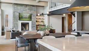 A spacious living area with a stone fireplace, a large dining table, and a staircase leading to an upper level.