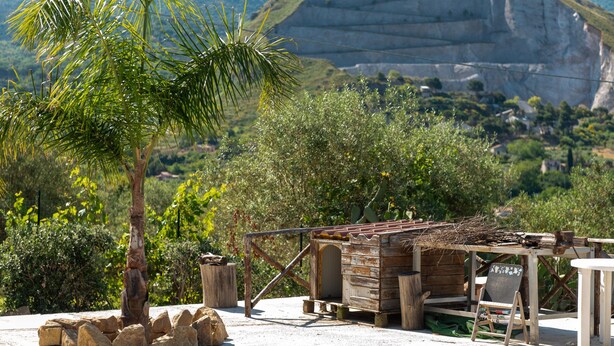A rustic wooden structure with a thatched roof, surrounded by rocks and greenery, set against a mountainous backdrop. - Casa Villa Aury — Cefalù, green oasis steps from the sea (Cefalù)