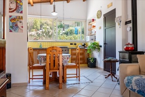 A kitchen with wooden chairs, a dining table, a window with a view of greenery, a stove, and a red pot on a black stove.