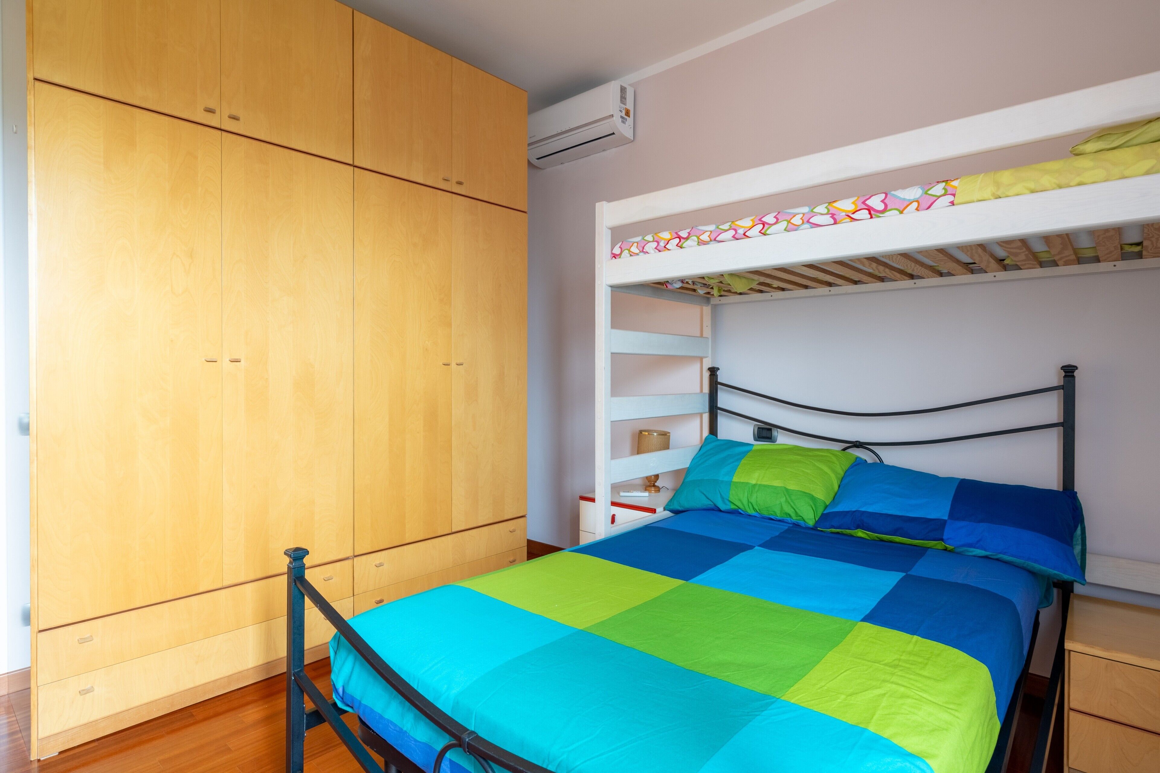 Un dormitorio con cama, armario de madera, estanterías empotradas y un equipo de aire acondicionado.