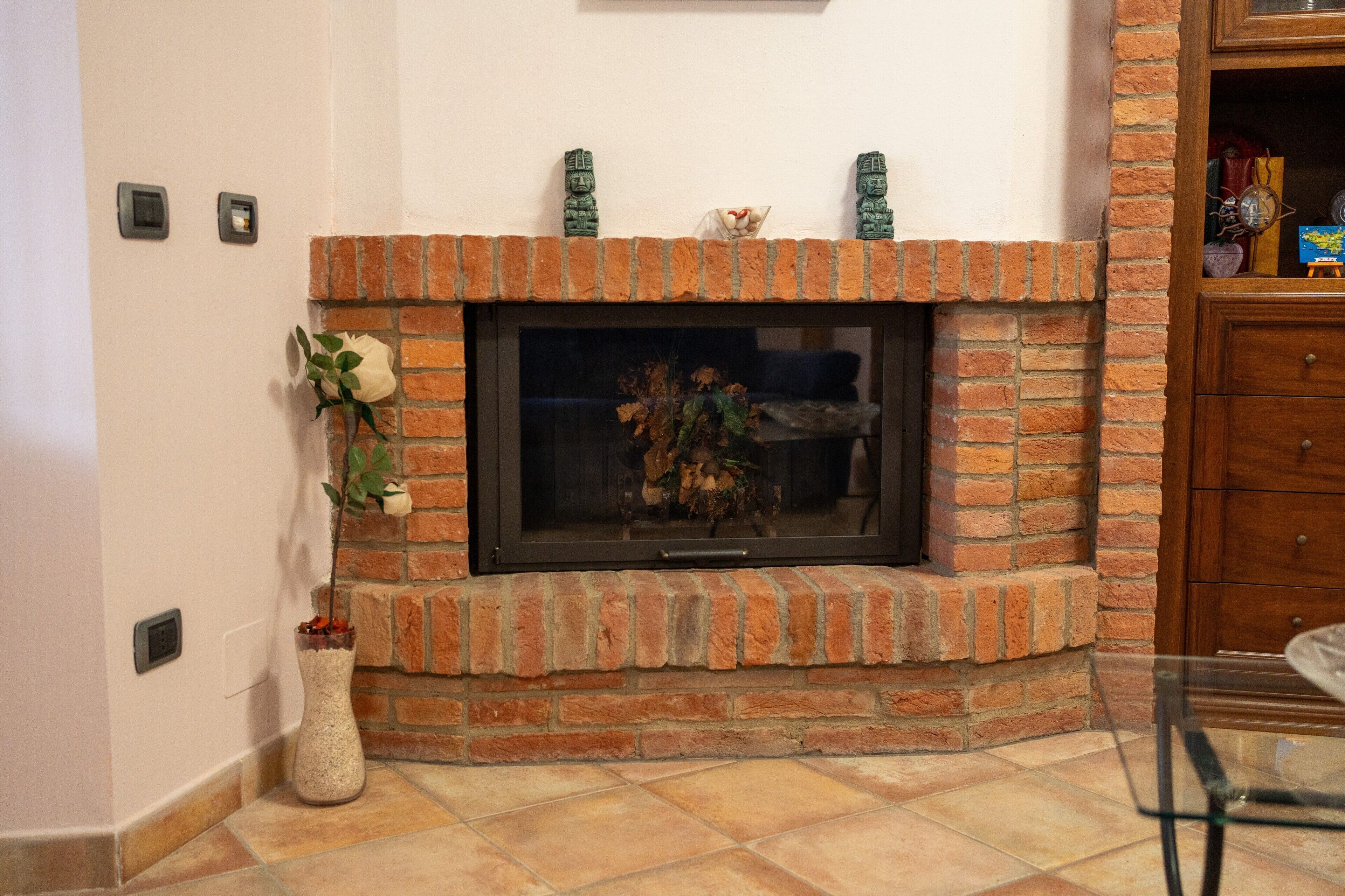 Una chimenea con revestimiento de ladrillo, un jarrón con una planta y una pequeña estatua encima.