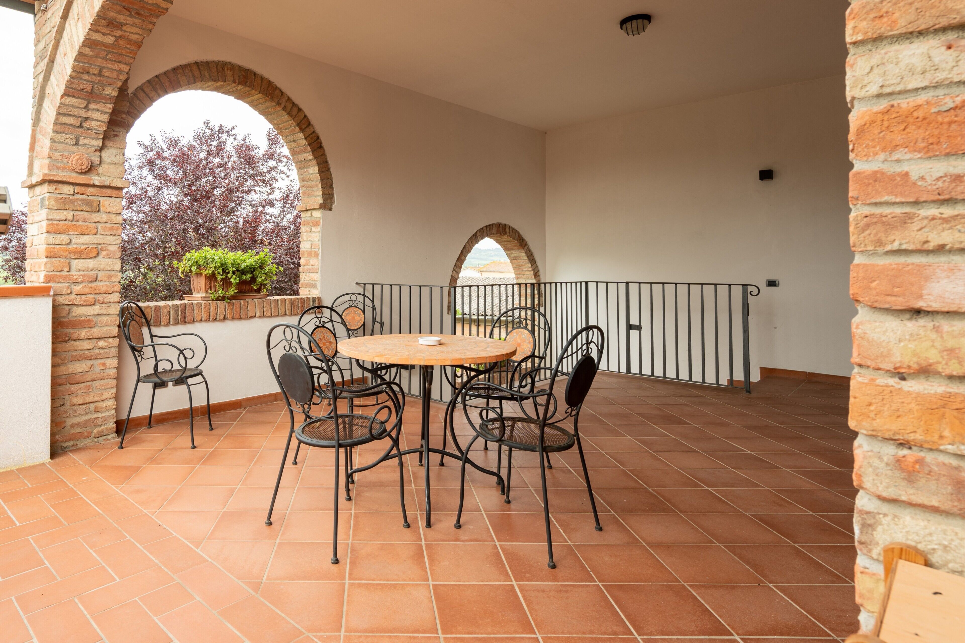 A covered patio with a round table and four chairs, brick walls, and arched doorways.