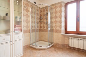 A corner shower with a glass door, beige patterned tiles, a wooden cabinet, and a radiator.