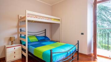 A bunk bed with a lower bed and a top bunk, a bedside table with drawers, and a window with a view of greenery.