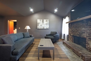 A living room with a sofa, armchair, coffee table, fireplace, and artwork on the wall.