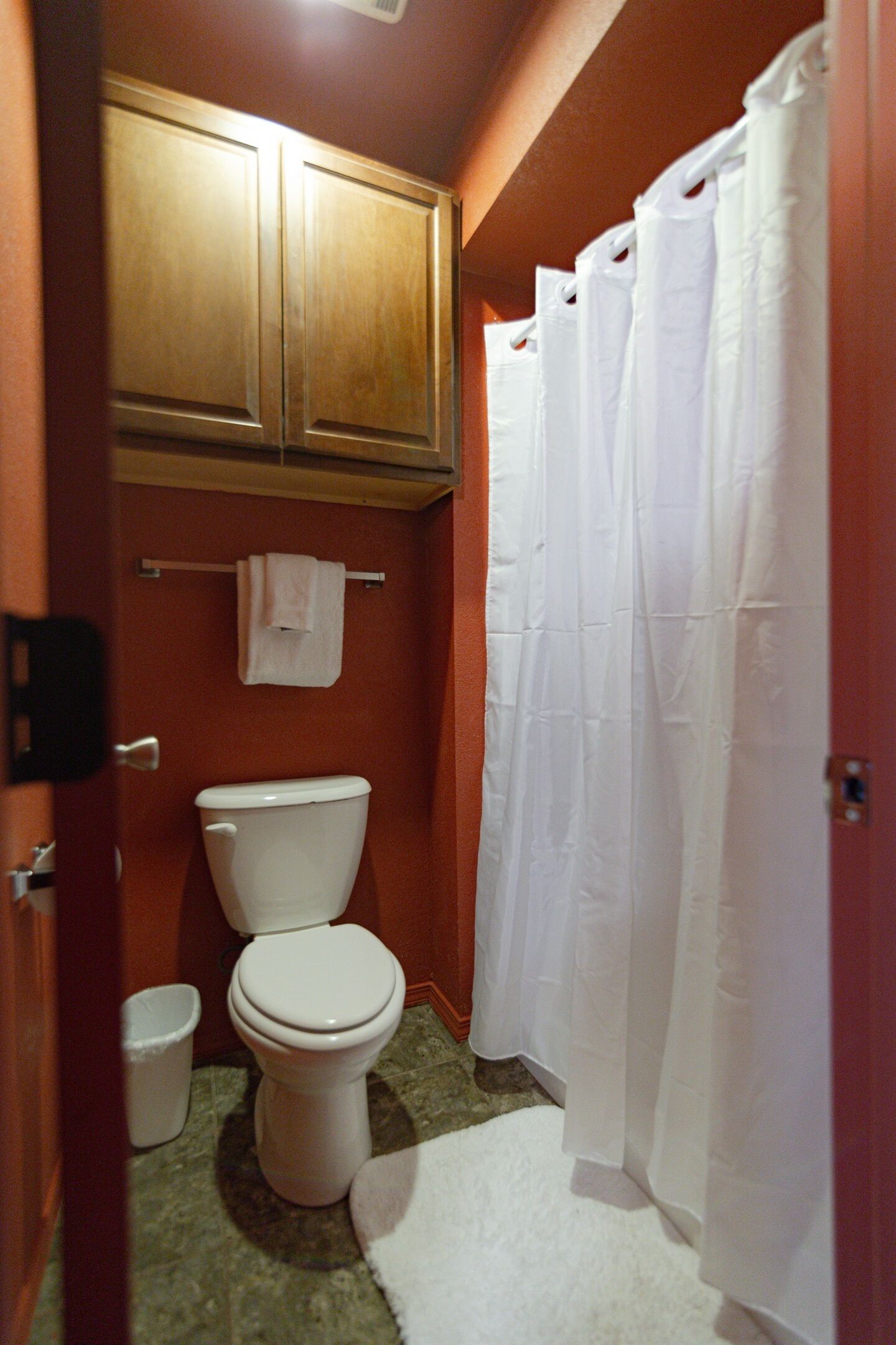 A bathroom with a toilet, a cabinet, a shower curtain, and a towel rack.