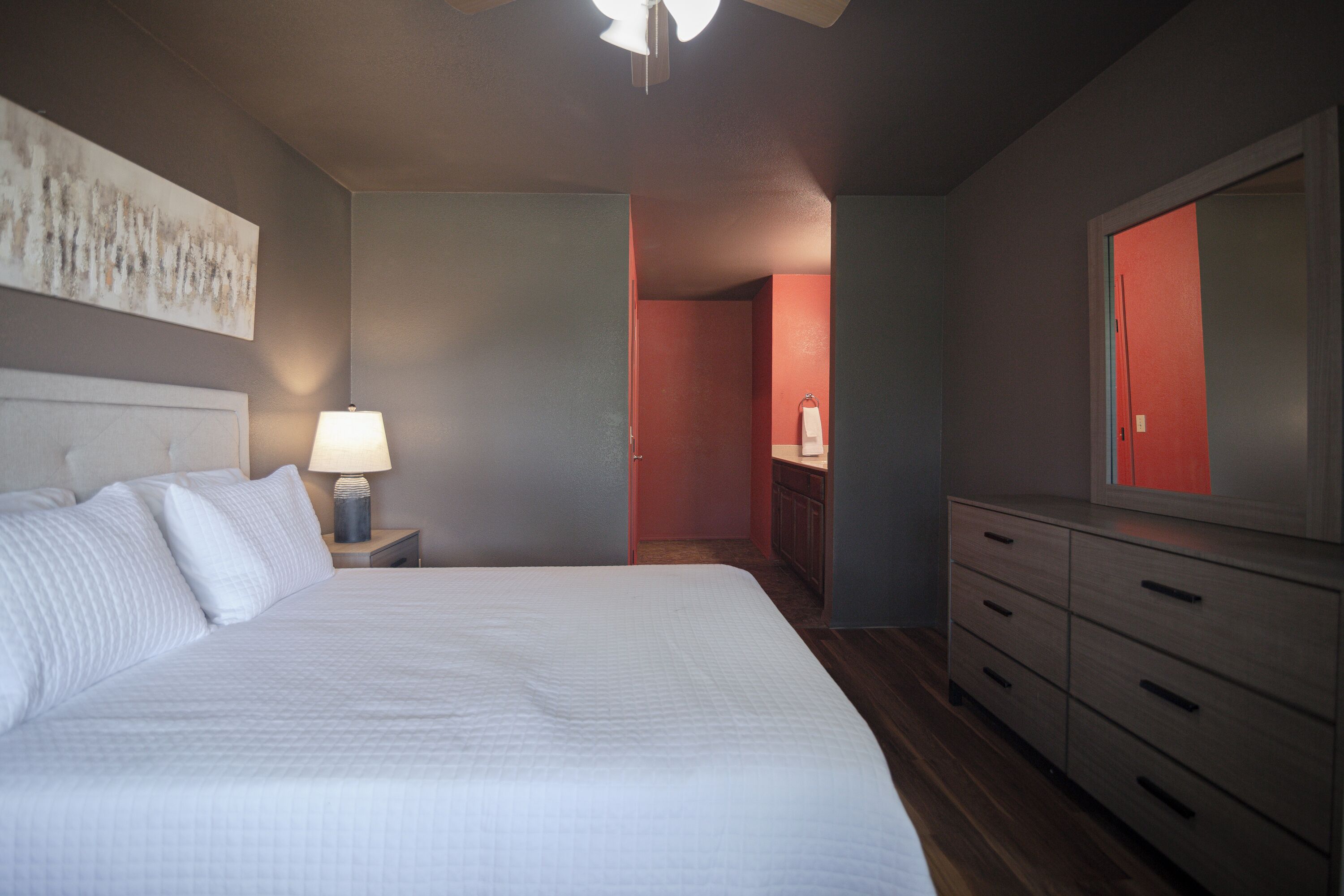 A bedroom with a bed, nightstand, dresser, and a mirror.