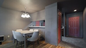A modern kitchen with a dining area, a red door, and a hallway leading to another room.