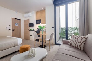 Una habitación de hotel con cama, sofá, una mesita, zona de cocina y balcón.
