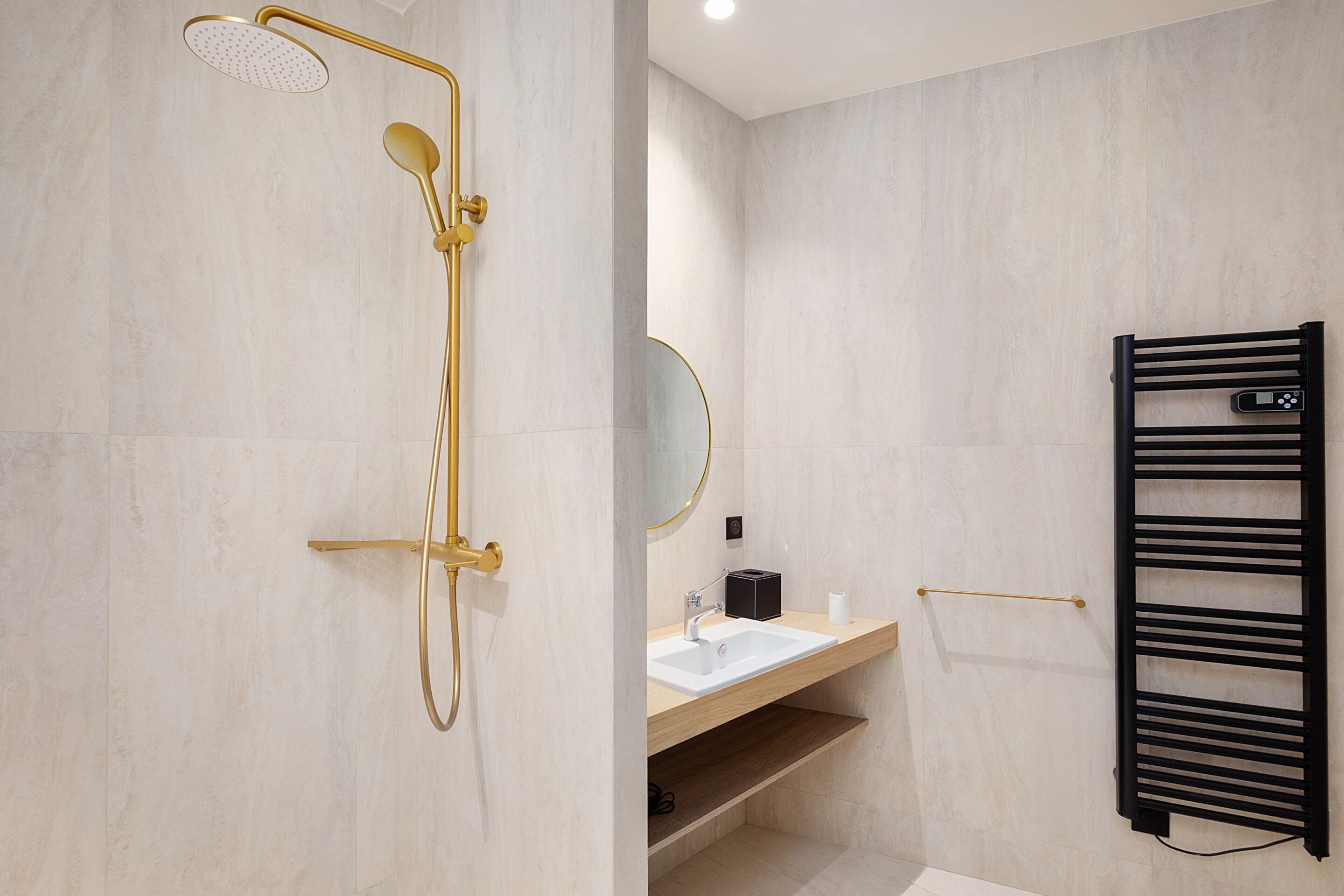 A modern bathroom with a gold shower, a white sink, a black towel rack, and a mirror.