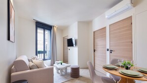 A modern living room with a sofa, a small table, a dining table set for four, and a TV mounted on the wall. - Maison Solférino  (Boulogne-Billancourt)