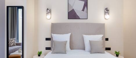 Una habitación de hotel moderna con una cama grande, dos mesitas de noche, un cabecero, una obra de arte abstracta colgada en la pared y un espejo que refleja parte de la habitación.