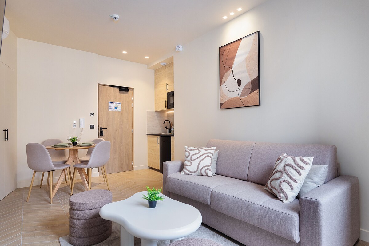 Una sala de estar moderna con un sofá, una mesa de comedor con sillas, una mesita blanca y una planta en maceta.
