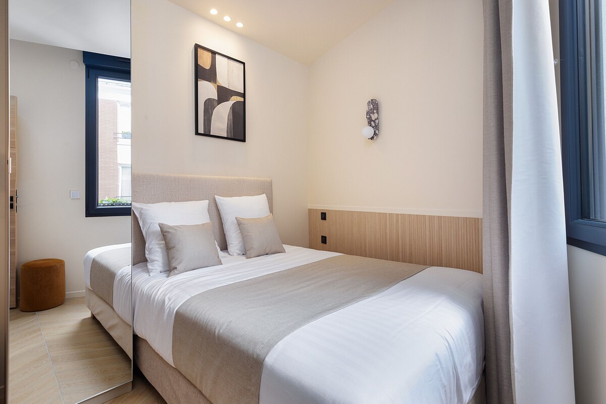 Un dormitorio moderno con una cama grande, una mesita de noche, una obra de arte en la pared y un ventanal con cortinas.