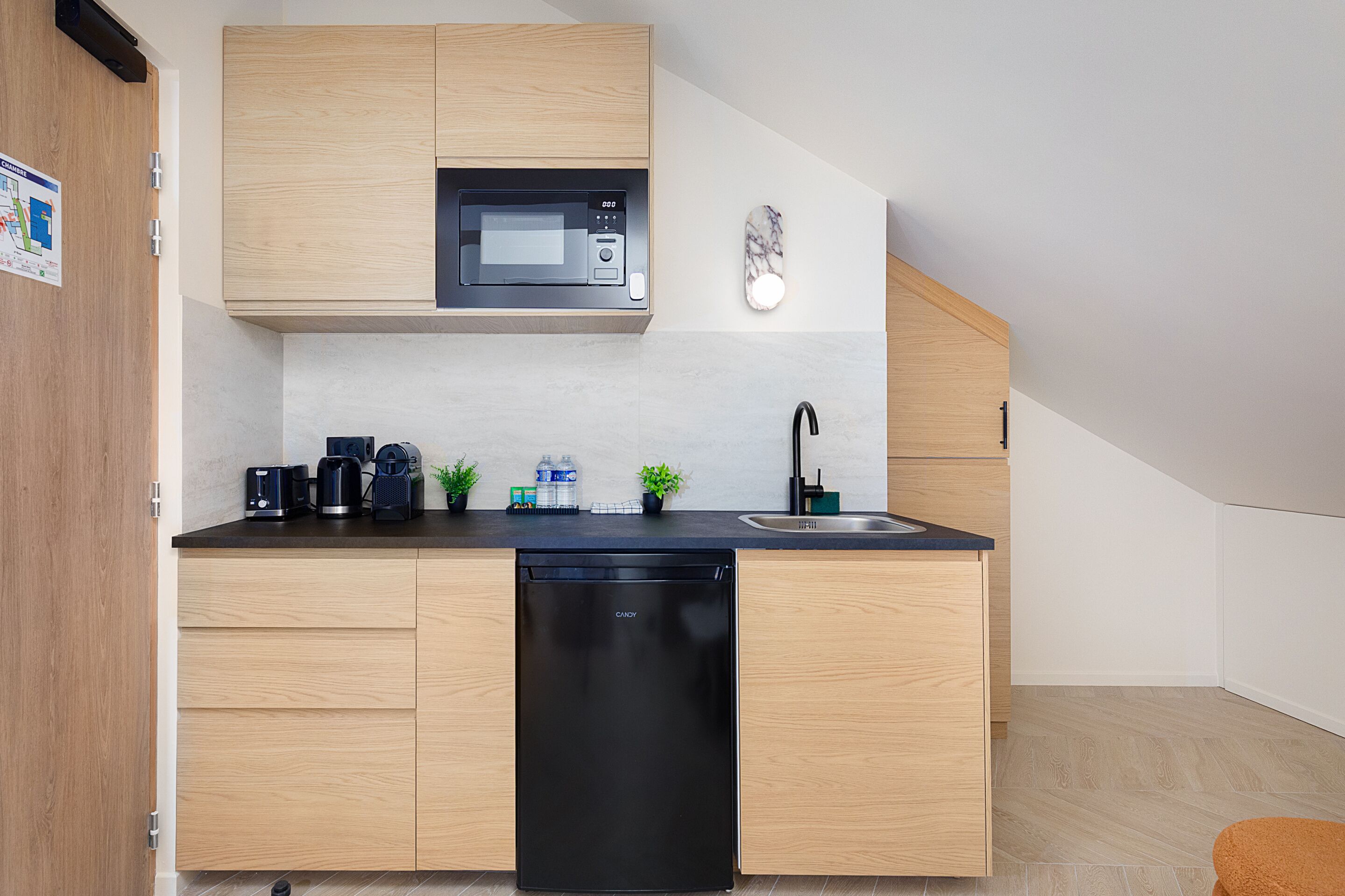 A modern kitchen with wooden cabinets, a black dishwasher, a microwave, a sink, and a small plant on the counter.