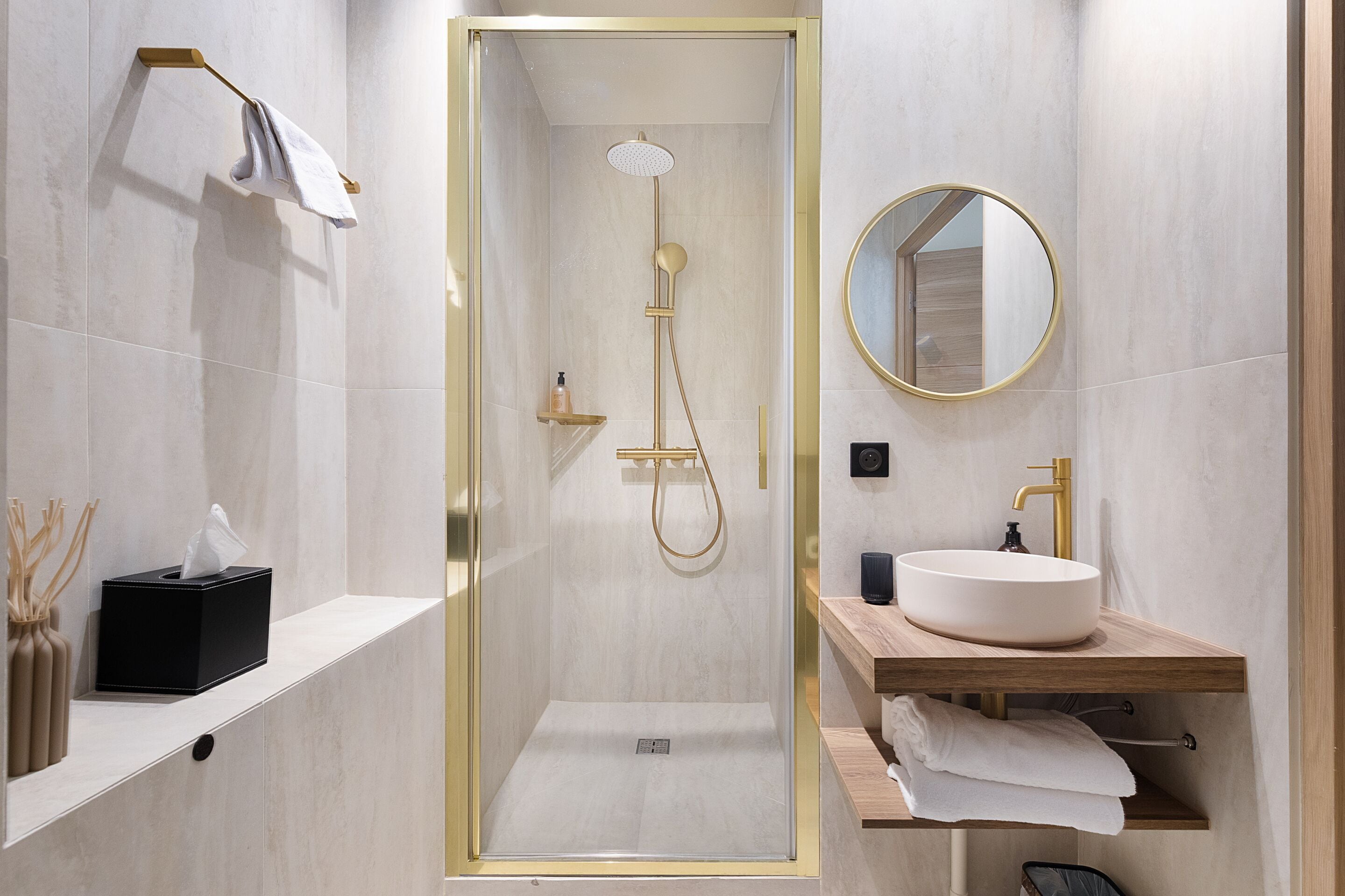 A modern bathroom with a glass-enclosed shower, a round mirror, a sink, and a towel rack.