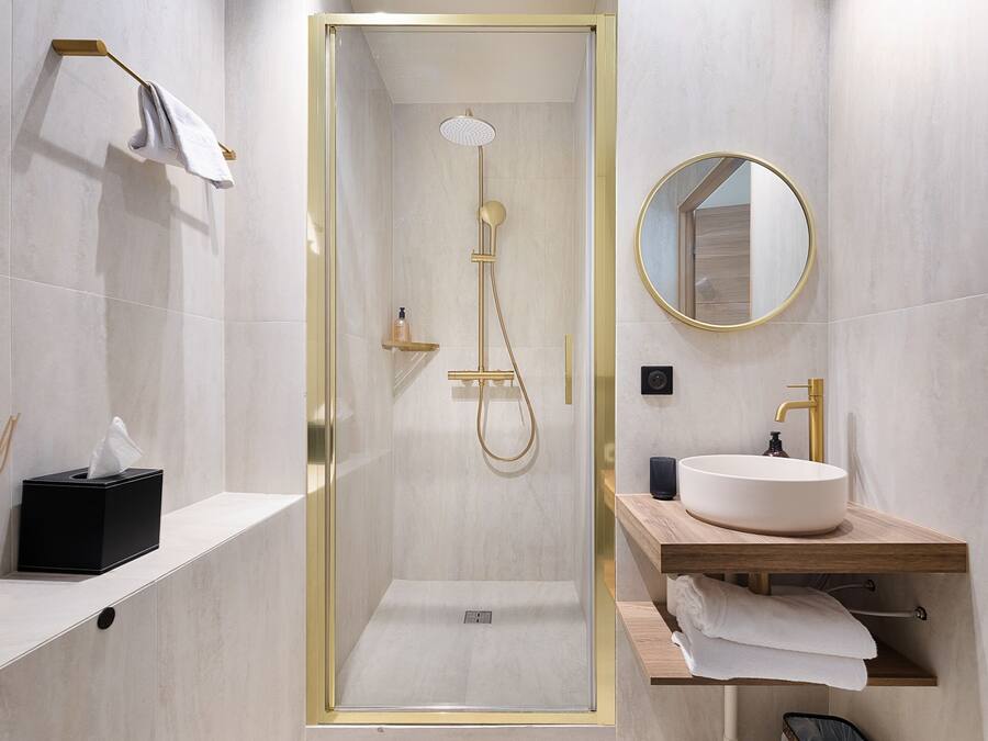 A modern bathroom with a glass-enclosed shower, a round mirror, a sink, and a towel rack.