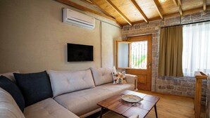 Un salon avec un canapé, une table basse, un téléviseur fixé au mur et un mur en pierre.