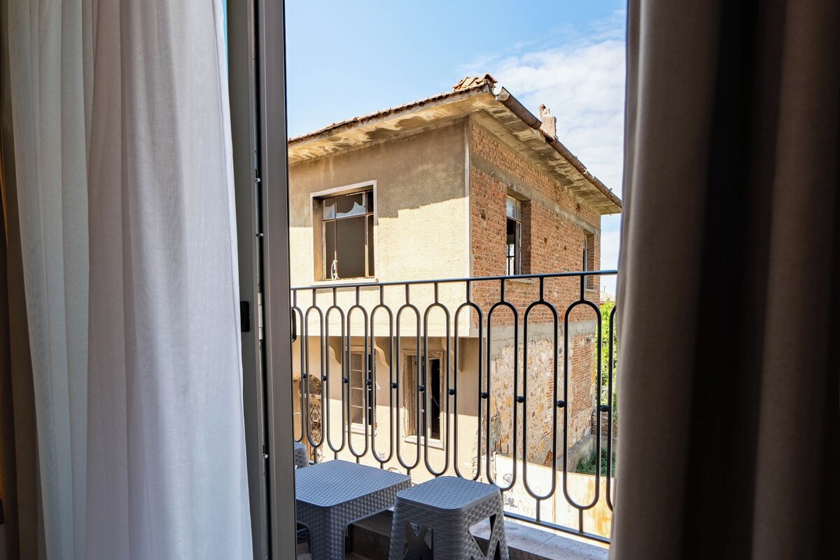 A balcony with a table and chairs, a view of a building, and a curtain partially drawn.